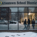 Students bundling outside the school entrance with snow‑covered parking lot and warm glow from inside.