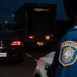Police cruiser parking beside a figure on the ground with Amazon logo on uniform and Amazon delivery van in highway dusk
