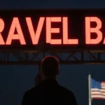 Person looking up at large digital screen with travel ban message and glowing American flag at border crossing