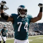 Brandon Graham raising arms in celebration with Eagles jersey and helmet while Washington logo appears on helmets behind him