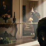 Police officer stands vigilantly beside crime scene tape with police cruiser parked and wilted flowers in foreground.