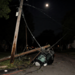 Broken power pole lying on street in Oxford Circle with flip-down car roof above it and downed wires across pavement.