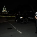 Police officer standing beside body with crime scene tape and black SUV in night street