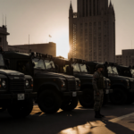 Soldier standing by a California National Guard vehicle with LA City Hall and sunset in background