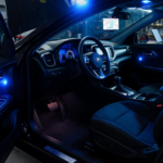 Car opening shows dark interior lit by blue police lights with exposed engine and technician nearby working on diagnostics