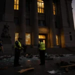 Allentown police patrol around a darkened federal courthouse with shattered windows glowing in sunset light.