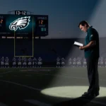 Coach Nick Sirianni standing on sideline holding playbook with spotlight and scoreboard 13-12