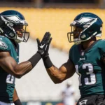 Quinyon Mitchell and Cooper DeJean high‑fiving after play with Philadelphia Eagles stadium lights and yellow seats scene