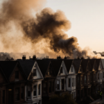 Firefighters battling blaze with bright yellow jackets against smoke-filled dawn sky and charred rooftops