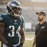 Jalen Carter Philadelphia Eagles tackle standing on the field with helmet and pads ready and Coach Sirianni watches nearby