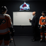 Coach studying playbook on whiteboard in Flyers locker room with empty spot for Cam York and Avalanche logo behind