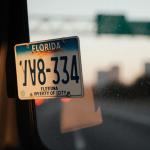 Florida license plate frame stuck on rental car window glowing with warm light and blurred highway at dusk.