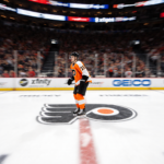 Flyers player standing alone on ice during shootout with swirling arena lights and Flyers logo in background