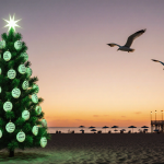 Green Christmas tree glowing on Jersey Shore beach at sunset with shells on branches and distant boardwalk.