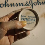Woman holding dusty baby powder container with stained fingers and faded logo in nostalgic glow