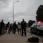 Students escorted away from buses with police and an abandoned backpack on the sidewalk