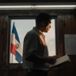 Kilmar Abrego Garcia standing in dim immigration office holding folder with hope near El Salvador flag