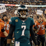 Jalen Hurts celebrates with teammates amid confetti and fans in orange jerseys and green jerseys with Philadelphia skyline be