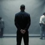 Joseph Cini standing with hands behind his back before a grey Philadelphia police backdrop showing a somber resignation.