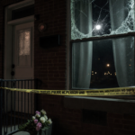 Police tape encloses front door with abandoned bouquet and broken window frame.