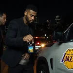 Suspect standing over SUV holding key with Lakers logo and police cruiser flashing lights behind.
