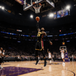 LeBron James shooting a three-pointer with warm glow from the basket and empty 76ers bench behind him.