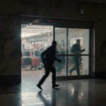 Security camera watches fleeing figure reflected in open sliding doors of empty Levi