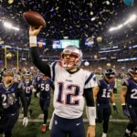 Mac Jones lifts football high with confetti and balloons while scoreboard shows 28-24 and defeated Ravens walk off field.