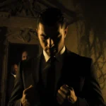 Mario Rodriguez standing in formal attire with clenched fists near a dimly lit mansion and vines and eyes down and golden lig