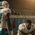 Miami Dolphins player Quinn Ewers stands on sidelines with Tua Tagovailoa dejected on bench and empty seats behind