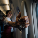 Passenger grasping airplane window handle with sky visible through open door and tense face