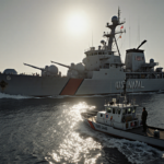U.S. naval vessel looming over oil tanker with grey-blue Caribbean Sea behind and Coast Guard cutter nearby.