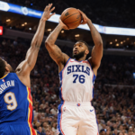 Paul George shooting over defender with bright blue Hawks jerseys and warm arena lights in background