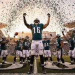 Eagles player raising arms with confetti swirling around him at victory celebration atop the 50‑yard line in golden sunset.