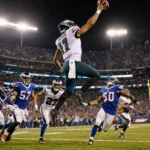 Jalen Hurts leaps throwing a touchdown pass to DeVonta Smith with Bills defenders scrambling behind and Eagles line charging.