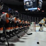 Empty Philadelphia Flyers bench with slumped players while scoreboard shows 5-3 Sabres and a goalie tends a puck in net