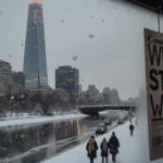 Snowflakes fall onto the frozen Schuylkill River in Philadelphia with the Comcast Center reflected in icy water and cars move
