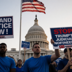 Protesters holding signs with blue attire and a flag near Capitol Building reading Demand Justice Now