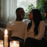 Raven‑Symoné laughing with Miranda Maday in dim living room with candles and greenery