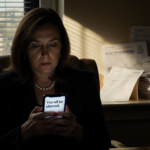 Rep. Chrissy Houlahan sits in dim office chair holding phone with morning light and stack of letters showing resilience while