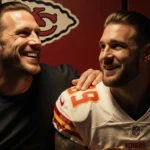 Rob Gronkowski sits beside Travis Kelce smiling with hand on shoulder in a dim Chiefs locker room.