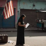 Mother looking at deportation notice with faded American flag and abandoned suitcase on El Salvador street