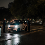 Police officers standing beside mangled Smart car with flashlights illuminating wet pavement