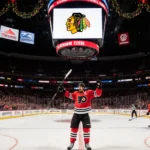 Flyers player lifts stick in victory on holiday-lit hockey ice with scoreboard showing Flyers logo