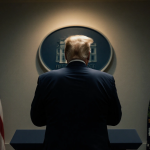 President Trump stands at a podium in the Oval Office with a faint glow from the presidential seal and a shadowy backdrop.