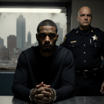 Tyvine Jones sits with cuffs on table and a marshal while Philadelphia skyline shows through a grimy window during interrogat