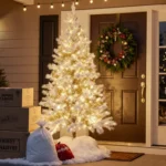 Artificial Christmas tree standing tall with fake snow bags and boxes labeled import tariffs near golden porch lights