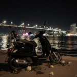 Scooter lying on its side with twisted metal frame and faint streetlight halo on the Venetian Causeway with neon glow