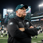 Vic Fangio stands on Eagles sideline with arms crossed and stadium lights shining on his focused face