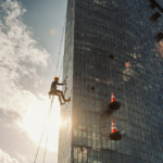 Alex Honnold climbing Taipei 101 ropeless with golden sun glow on glass and construction cones.
